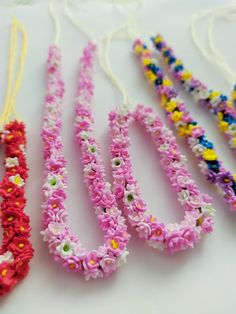 four necklaces made out of flowers on a white table with strings attached to them