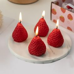 four strawberries on a plate with candles in the shape of pears