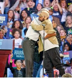 two people hugging each other while standing in front of a crowd with signs and microphones