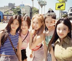 group of young women standing next to each other in front of a street sign and palm trees