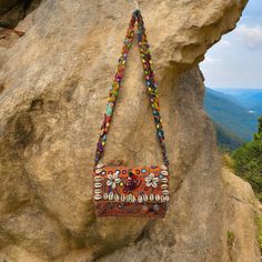 a handbag hanging from the side of a rock on top of a mountain with mountains in the background