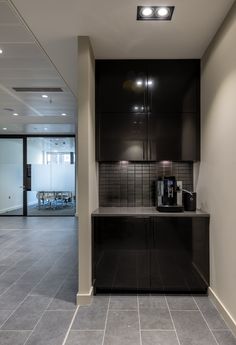 a kitchen with black cabinets and tile flooring next to a dining room table in an office building