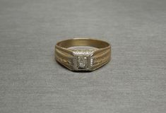 an old gold ring with a diamond in the center on a gray surface, showing that it has been worn for years