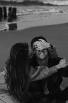 a man and woman sitting on the beach with their arms around each other as they kiss