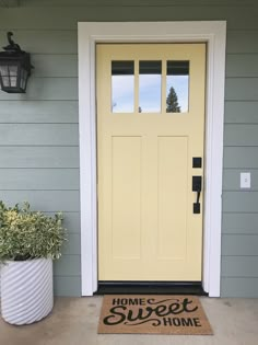 a yellow door with the words home sweet on it and a planter next to it