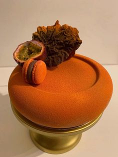 an orange cake sitting on top of a gold pedestal with a piece of fruit in the middle