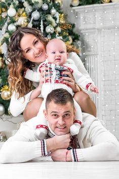 a man and woman holding a baby in front of a christmas tree