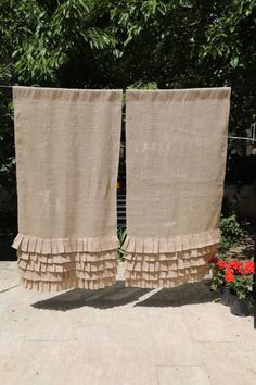 two towels hanging on a clothes line in front of some trees and flowers with red flowers behind them