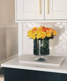 a vase filled with yellow roses on top of a white counter next to cupboards