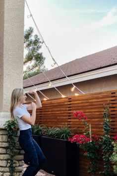 a woman leaning against a wooden fence with string lights hanging from it's sides