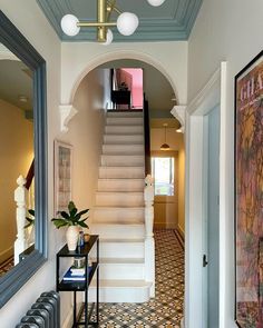 a hallway with stairs and tiled flooring next to a painting on the wall in front of a mirror