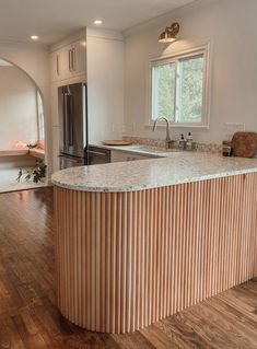 a large kitchen with an island in the middle and wood flooring on the other side