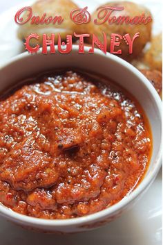 a white bowl filled with sauce next to some bread on a plate and the words onion & tomato chutney written in red