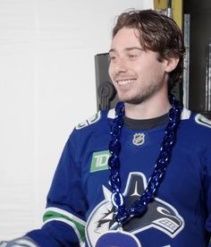 a man in a blue jersey is smiling and wearing a necklace that has a hockey puck on it