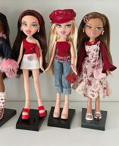 three dolls are standing next to each other on small black bases, one is holding a purse and the other two are wearing red