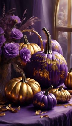 purple and gold painted pumpkins sitting on a table with flowers in front of them