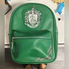 a green harry potter backpack sitting on top of a desk next to a pair of brown shoes