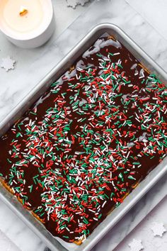 a chocolate cake covered in sprinkles on top of a table next to a candle