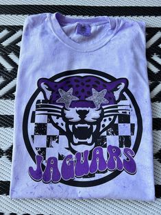 New product- Preppy Jaguars Mascot Shirt! Each shirt is meticulously printed by me using high-quality materials on a Comfort Colors shirt, known for its exceptional comfort and durability. Whether you're cheering on the Jaguars at the stadium or simply want to showcase your school spirit in your everyday attire, this shirt is the perfect choice. Available in Unisex sizes S to 3X, we've got you covered regardless of your preferred fit. The Preppy Jaguars Shirt features a classic crew neck and short sleeves with a fun splatter print! This preppy Jaguars shirt is a definite conversation starter and a unique fashion statement- wear it with jeans, shorts, or leggings for a casual and trendy look that showcases your Jags spirit! Note: As each shirt is individually printed, slight variations in c Cheap Shirt With Funny Print For School Spirit, Purple School Spirit T-shirt With Graphic Print, School Spirit Cotton Shirt With Graphic Print, Cotton School Spirit Shirt With Graphic Print, Purple Cotton Shirt With Sublimation Print, Trendy Purple Shirt With Graphic Print, Purple Cotton Shirt With Custom Print, Purple Cotton Top With Sublimation Print, Cotton Purple Top With Sublimation Print