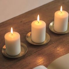 three white candles sitting on top of a wooden table