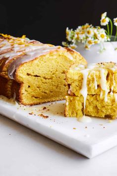 a loaf of pumpkin bread with icing on a white plate next to a bowl of flowers