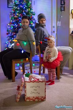 two adults and a child sitting in front of a christmas tree