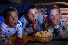 three young children are watching tv while eating popcorn