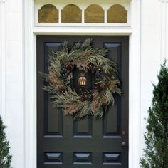 a wreath on the front door of a house with evergreens and pine cones around it