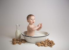 a baby sitting in a bowl with cookies and milk