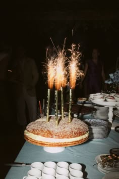 a cake with sparklers on it sitting on top of a table covered in plates and cups