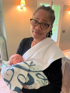 a woman holding a baby in her arms and looking at the camera while wearing glasses