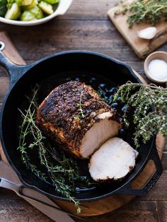 a pork roast in a cast iron skillet with herbs and garlic on the side