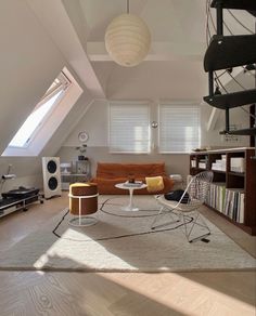 a living room filled with furniture and a spiral staircase in the background, under a slanted skylight