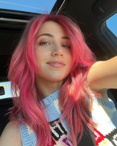 a woman with pink hair sitting in the back seat of a car and looking at the camera