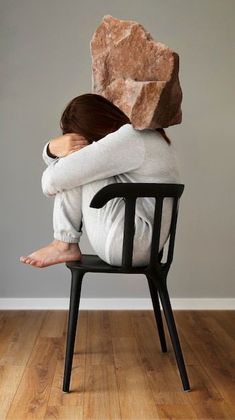 a woman is sitting in a chair with a rock on her head and hands behind her back