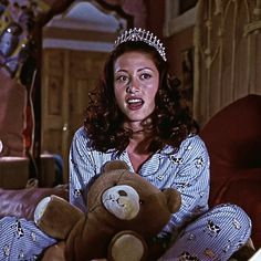 a woman wearing a tiara and holding a teddy bear in her lap, smiling at the camera