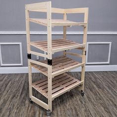 a three tiered wooden shelf on wheels in front of a gray wall and wood floor