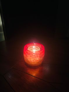 a lit candle sitting on top of a wooden table next to a glass container filled with liquid