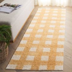 a yellow and white rug on the floor in front of a couch with a potted plant next to it