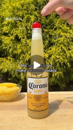 someone is holding a cherry in front of a bottle of corona liquid on a table