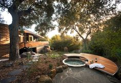 an outdoor hot tub in the middle of a garden with trees and rocks around it