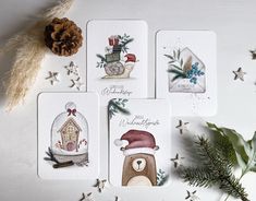 four christmas cards with bear and snowman designs on them next to evergreen branches, pine cones and star decorations