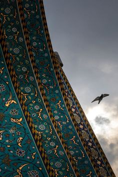 a bird flying in the sky next to a tall building with designs on it's sides