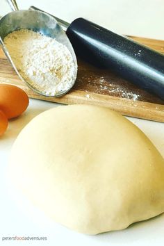 an uncooked ball of dough next to eggs and a rolling pin on a cutting board