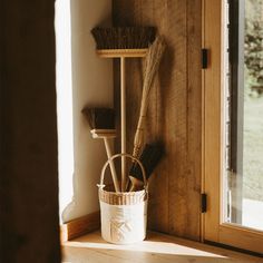 brooms and brushes are sitting in a basket on a shelf next to a window