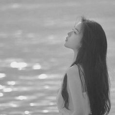 a woman standing on the beach looking up at the sky with her hair blowing in the wind