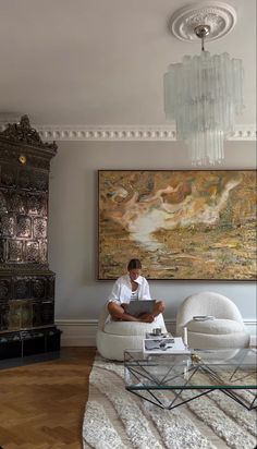 a man sitting on a white chair in front of a painting and coffee table with a glass top