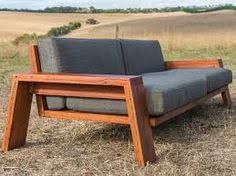 a couch sitting on top of a dry grass field next to a wooden frame chair