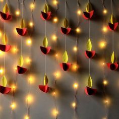 several red and yellow paper flowers are hanging from strings with string lights on the wall