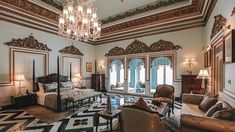 an ornate bedroom with chandelier, bed and two couches in front of windows